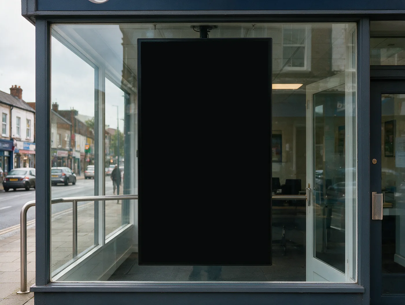 Shaded shop window on an overcast UK high street with one 55-inch portrait digital display behind the glass